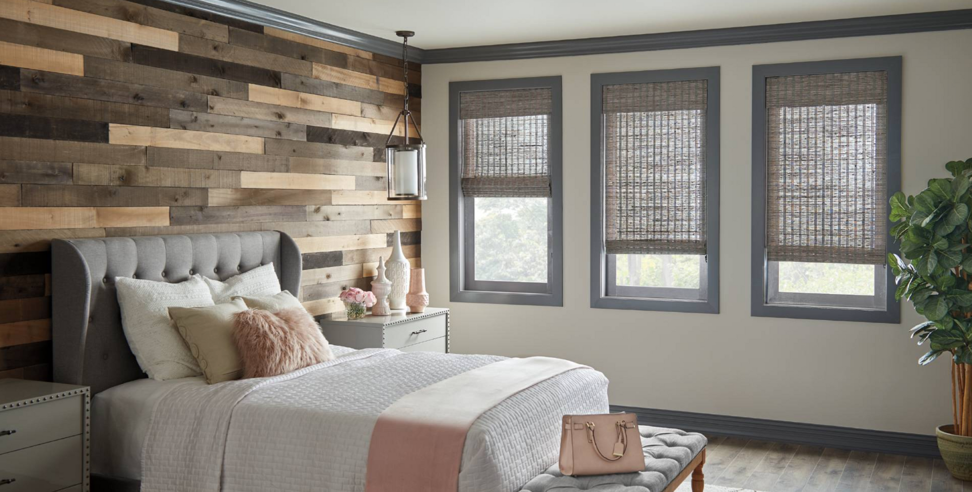 Bedroom with wood accent wall, bed, and three windows with shades.