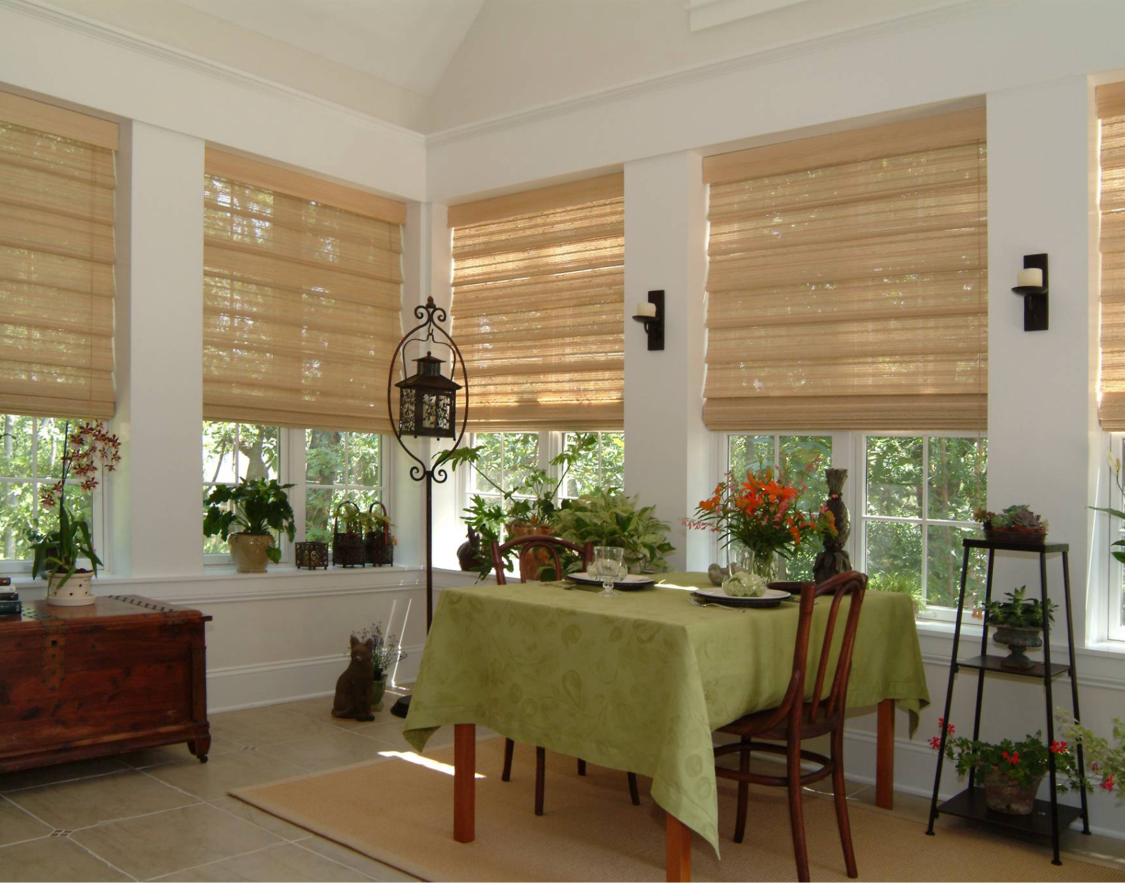 Sunroom with woven blinds, dining table set for two, and plants by the windows.