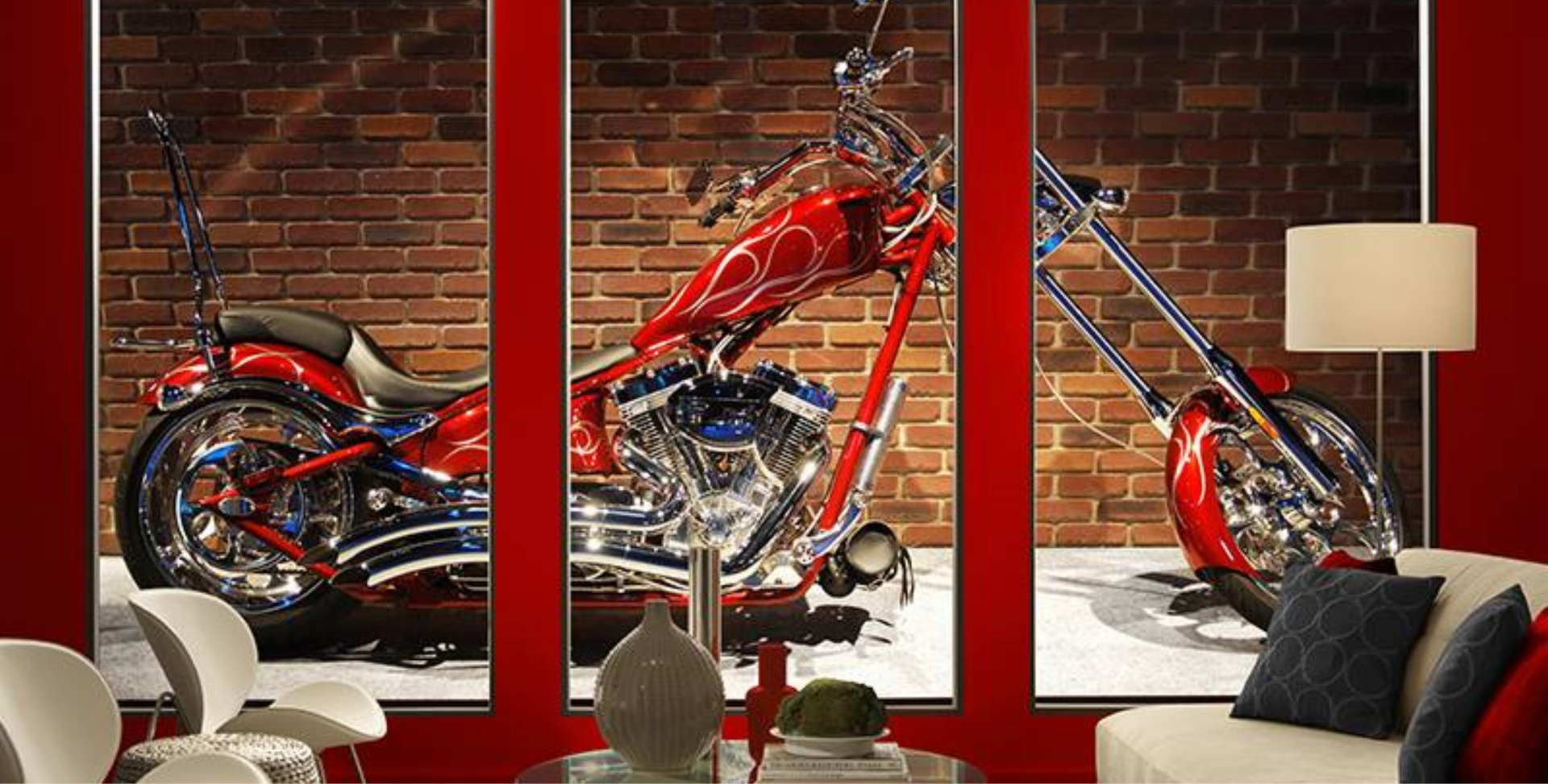 Red motorcycle displayed on a brick wall, three-panel artwork with red frames above a red table and white furniture.