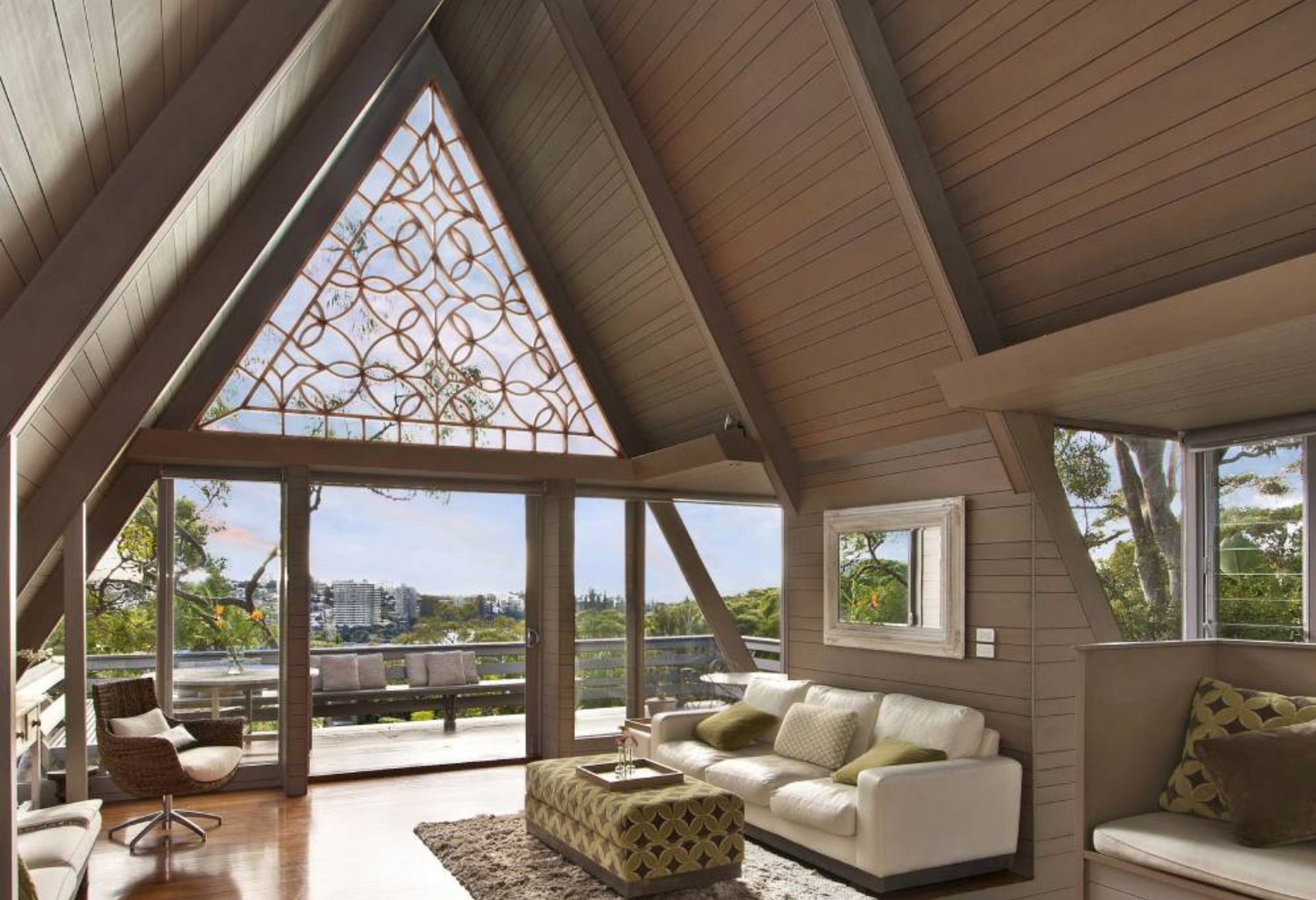 Living room with triangular window, white sofa, and view of outdoor seating.