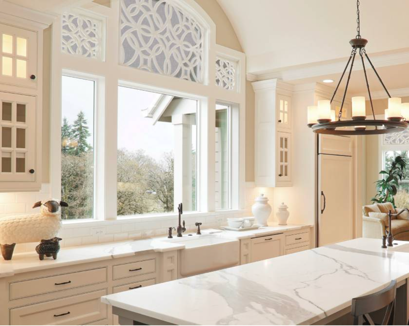 White kitchen with large window overlooking a yard; island with countertop, chandelier.