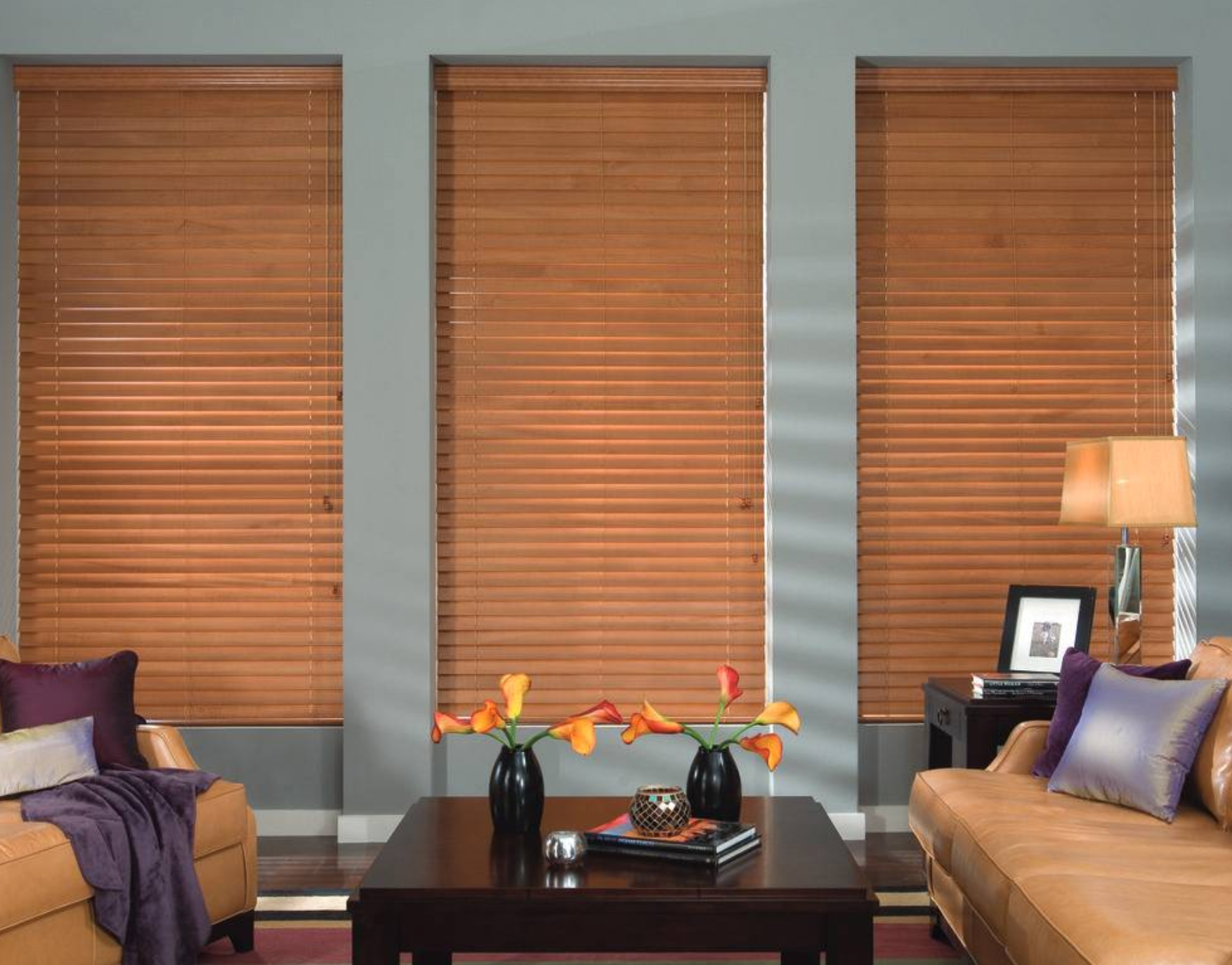 Three windows with closed wooden blinds in a living room; brown furniture and decor.