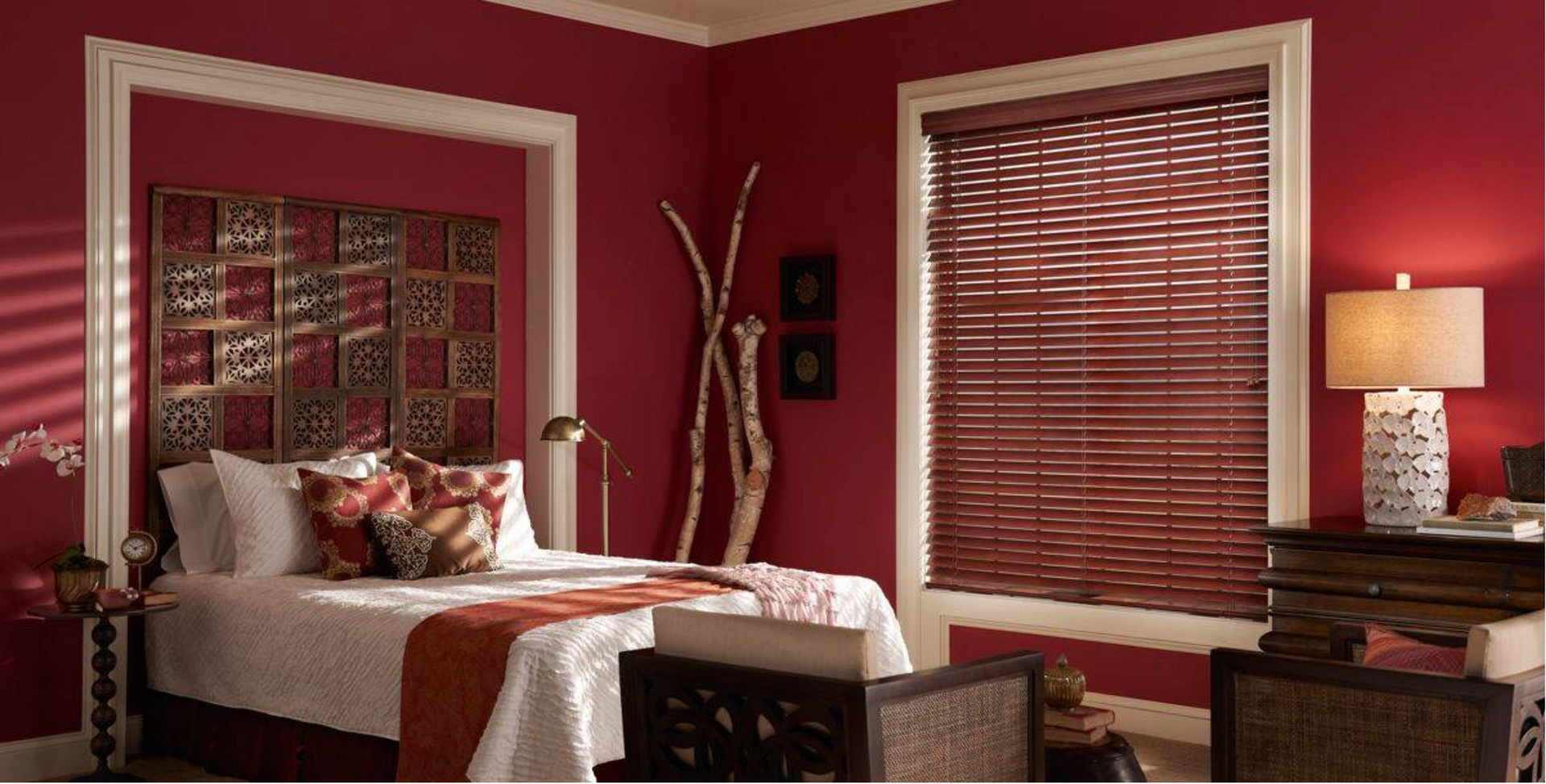 Bedroom with a red wall, wooden blinds, bed, nightstand, and decorative headboard.