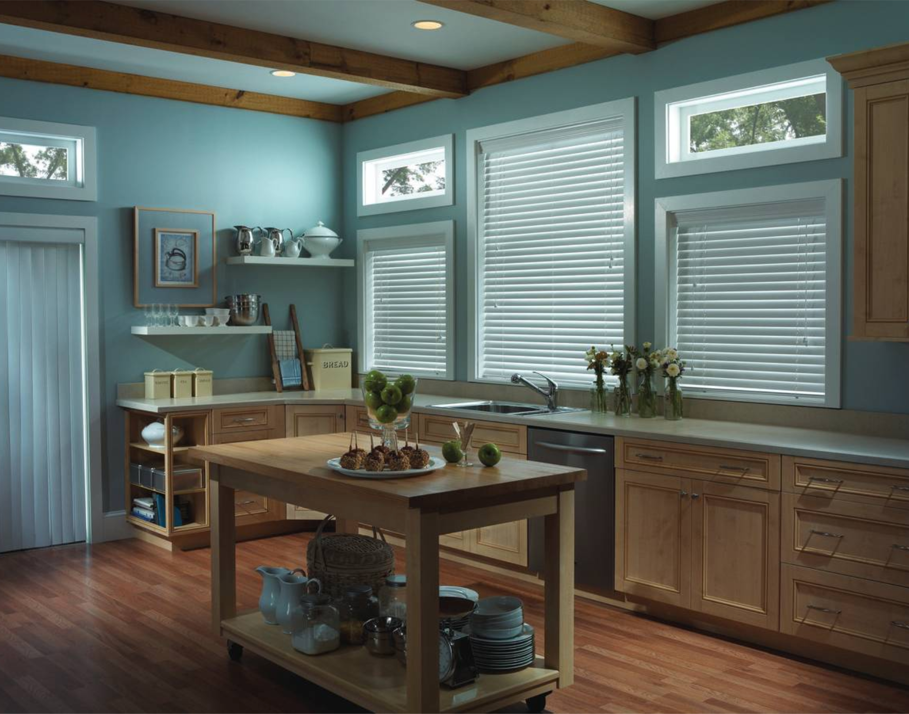 Kitchen with blue walls, wood cabinets, and large windows with blinds. A wooden island and shelves are visible.