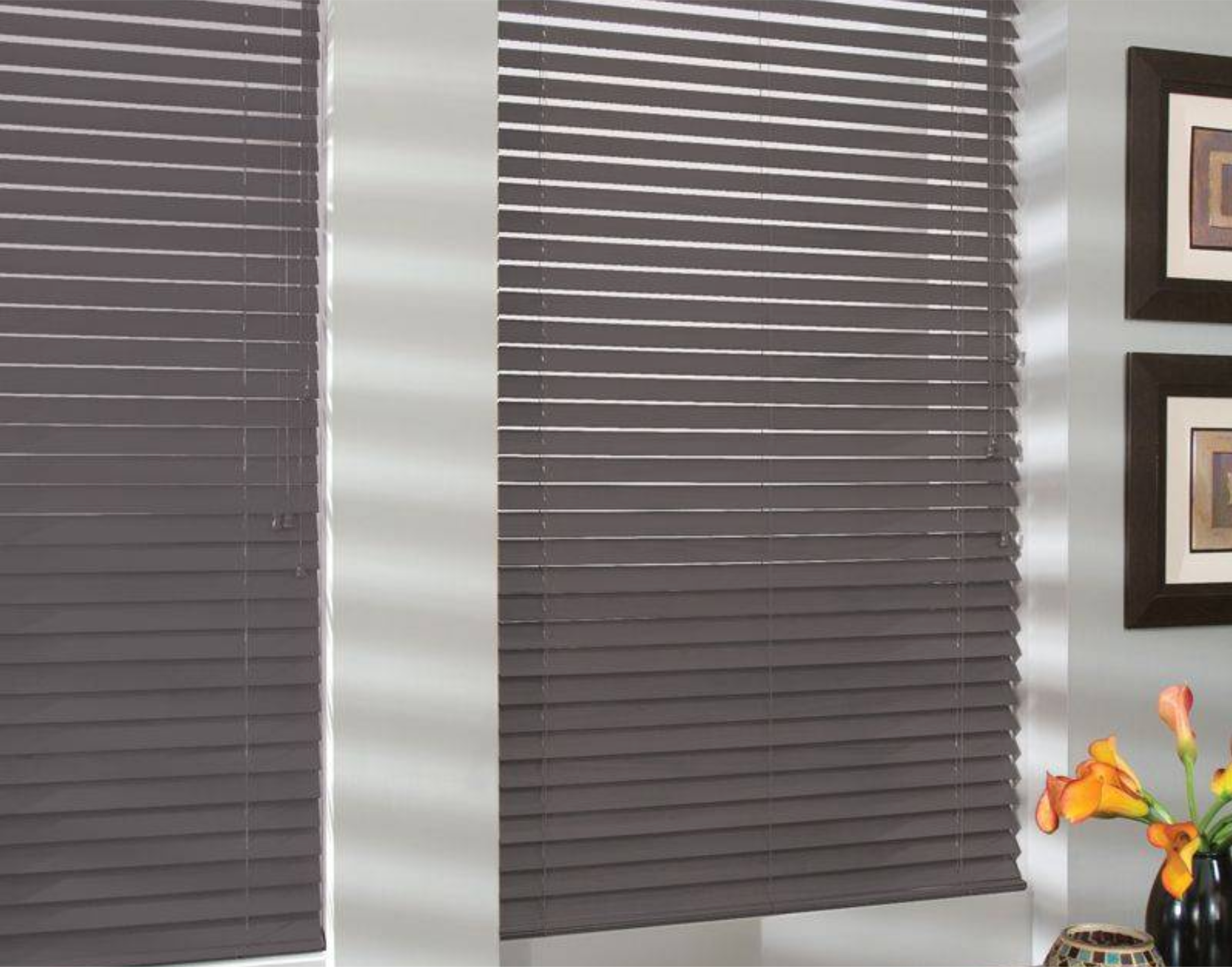 Gray horizontal blinds on windows, partially open, with sunlight and artwork visible.