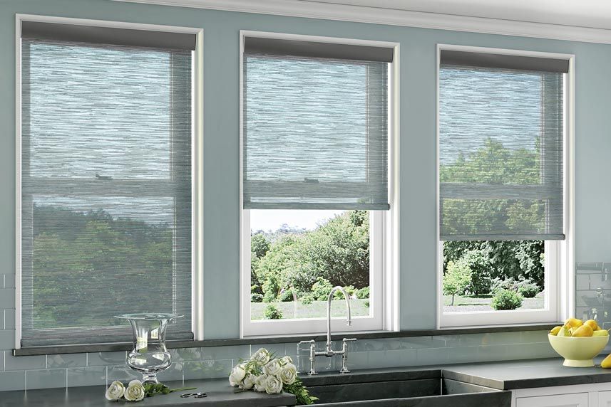 Three windows with light blue woven shades in a kitchen, overlooking a sunny outdoor scene.