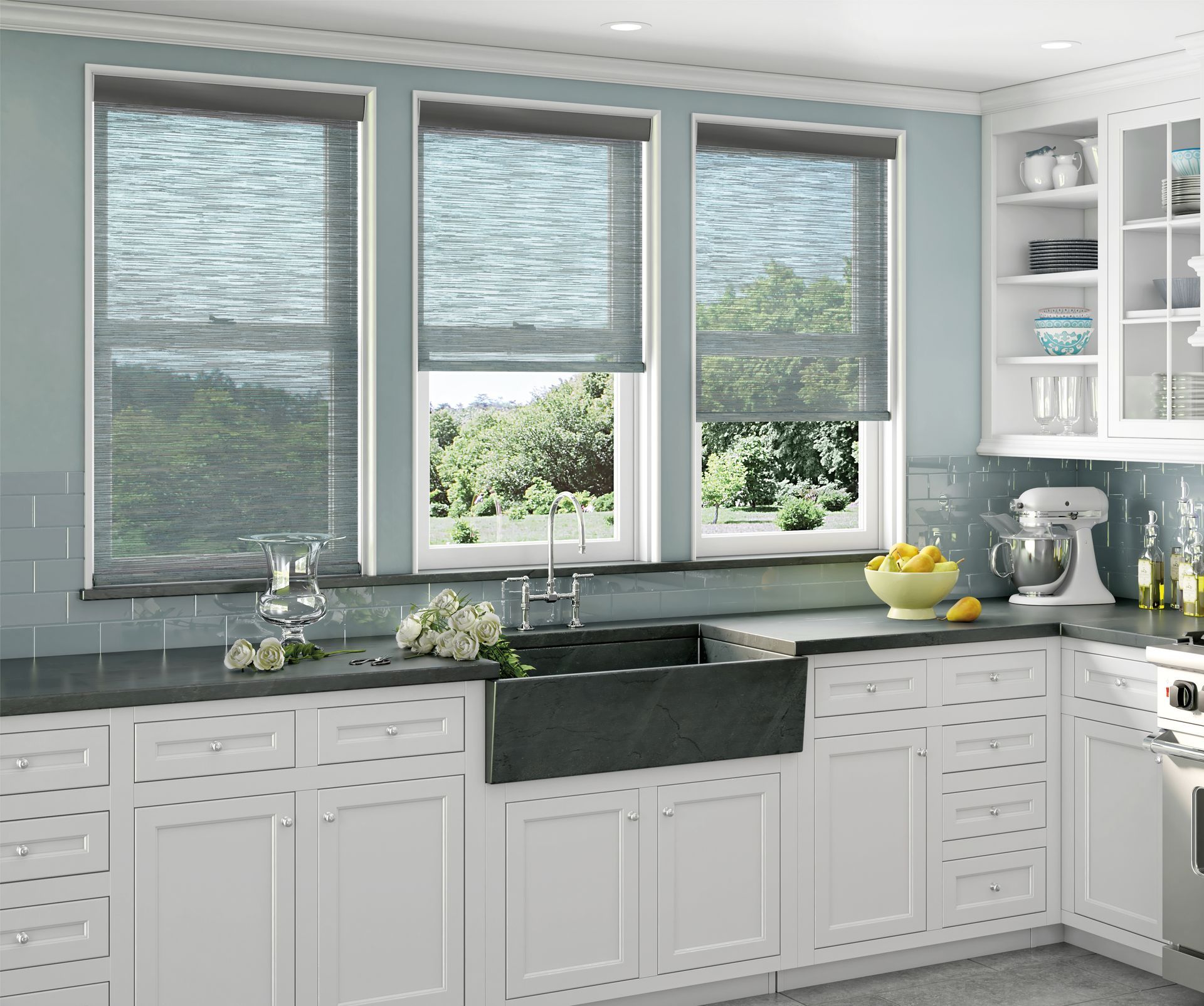 Kitchen with three windows, white cabinets, dark sink, and blue wall. Roller shades are down.