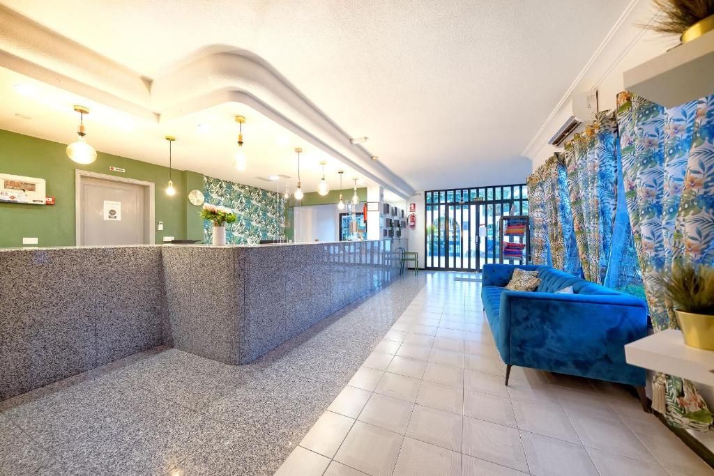 A hotel lobby features a long, granite-topped reception desk, a blue velvet couch, and large windows with floral curtains.