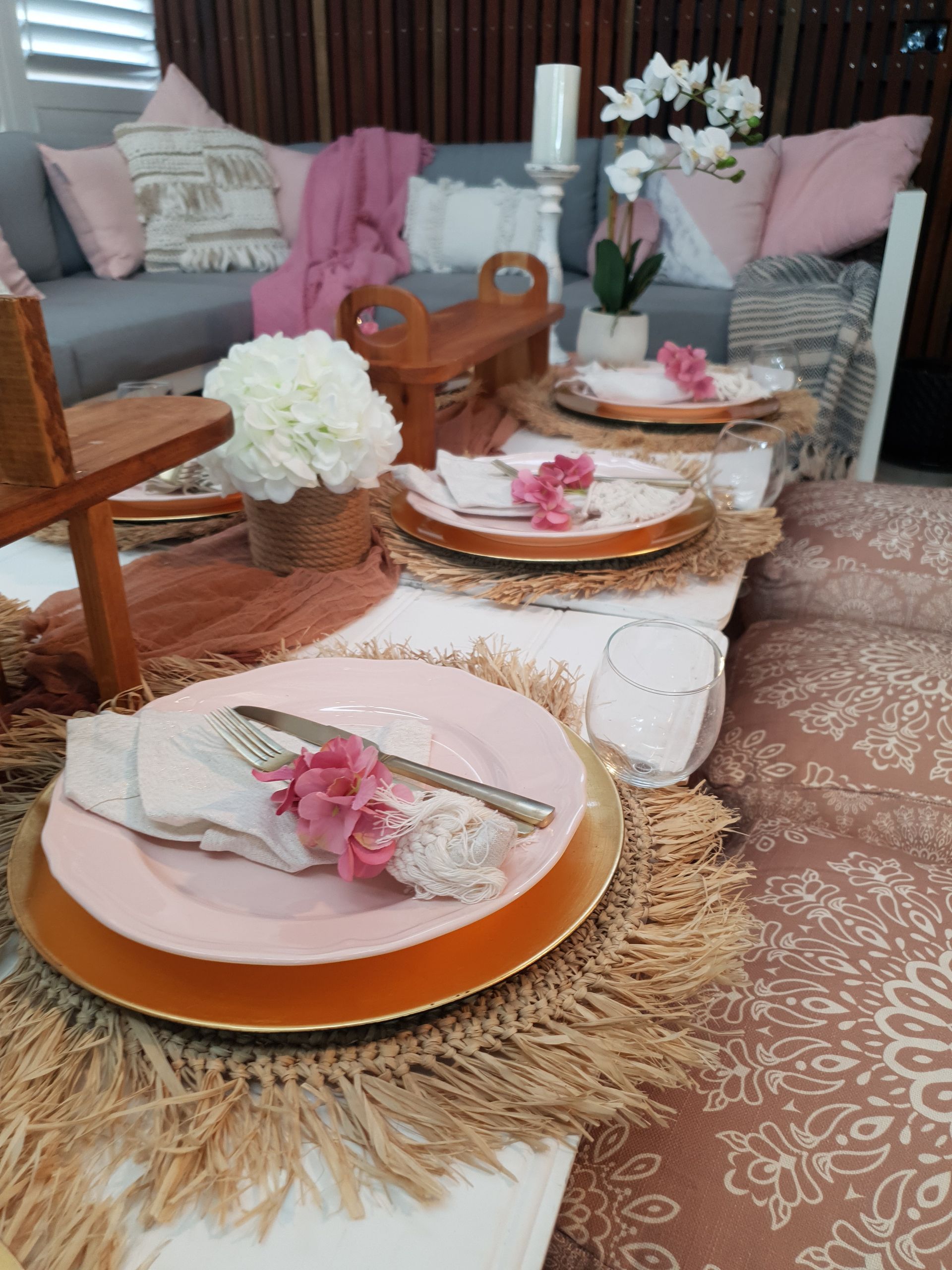 A decorated table setting with pink plates, gold chargers, and floral accents in an outdoor setting.