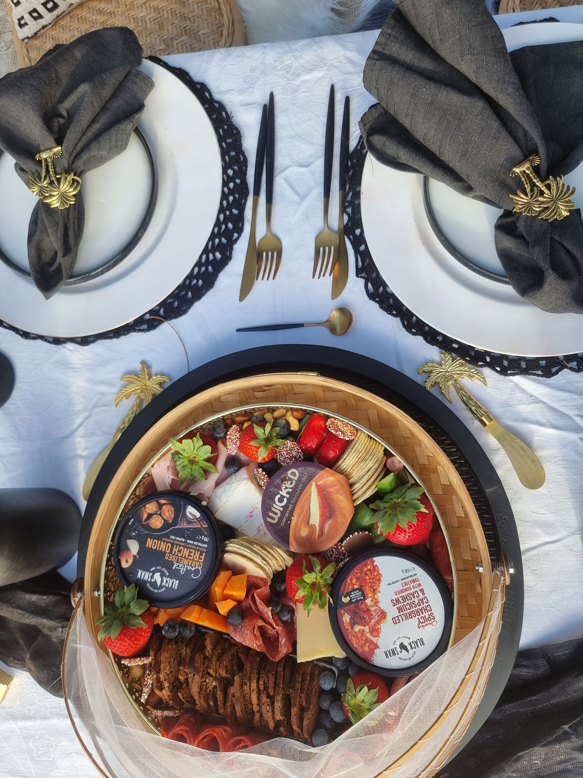 Table setting with charcuterie board, white plates with black trim, black napkins, gold silverware, and food.