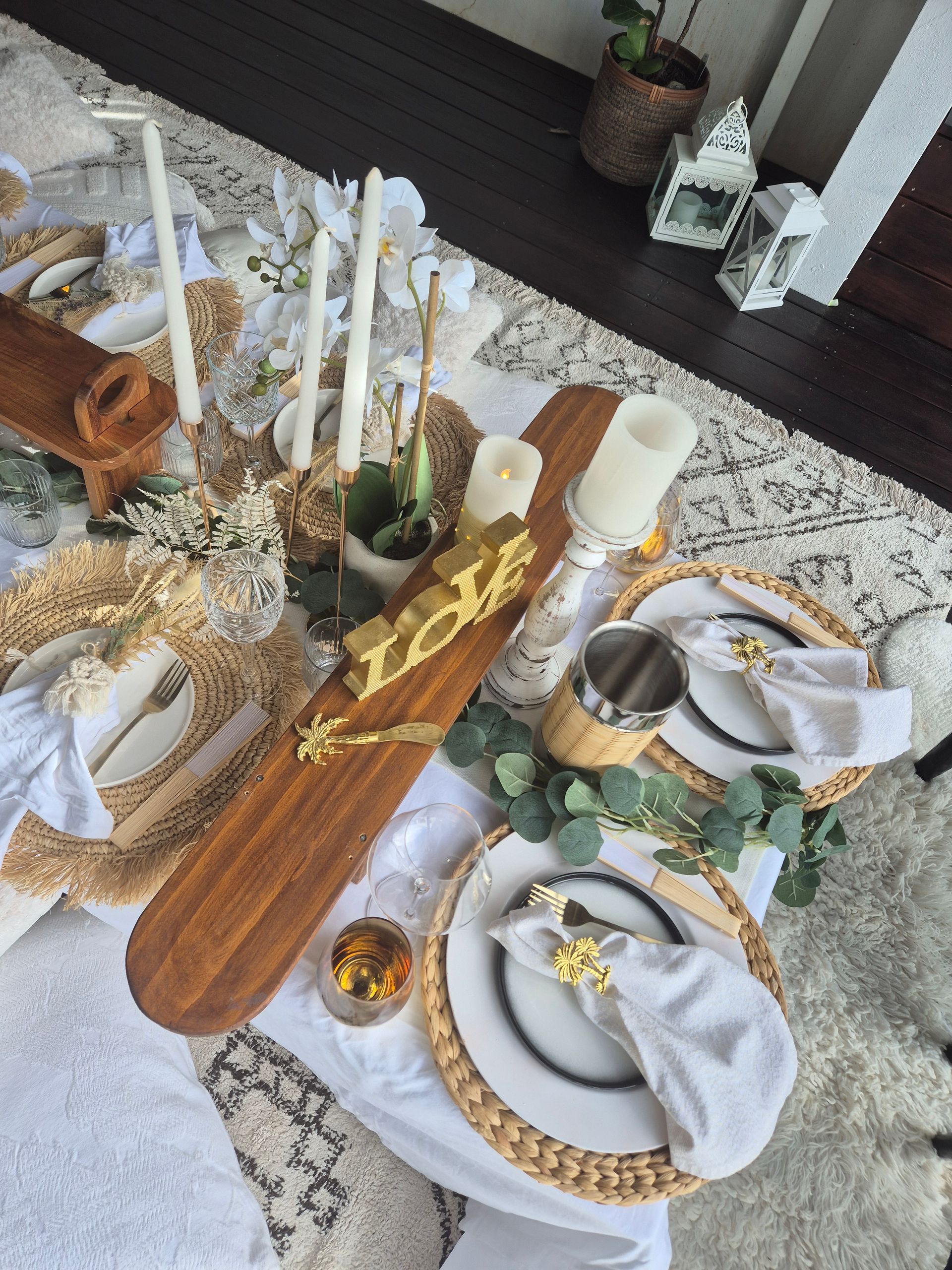 Elegant outdoor table setting with gold accents, candles, and white plates.