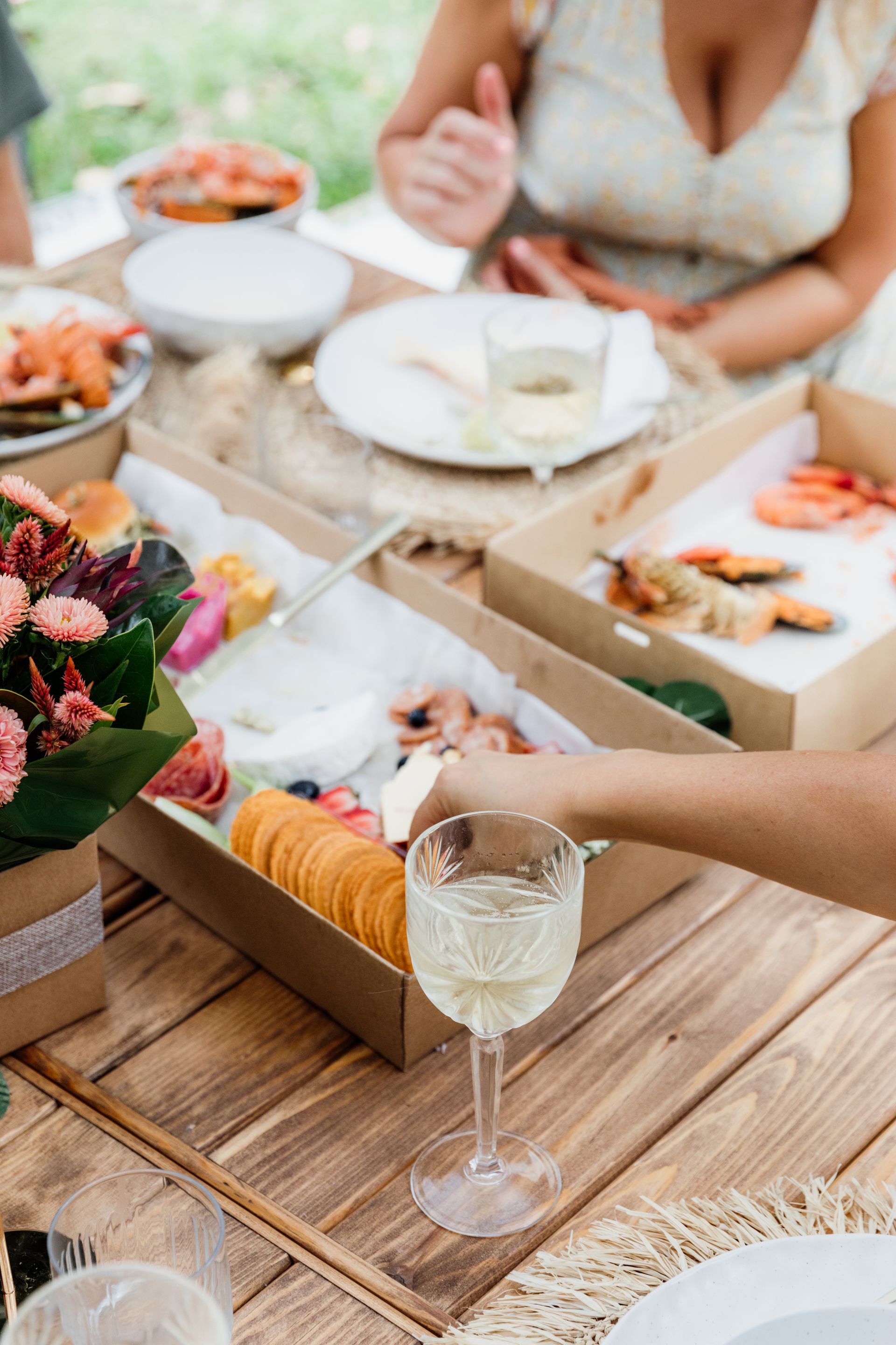 Picnic table with charcuterie, seafood, and a glass of white wine.