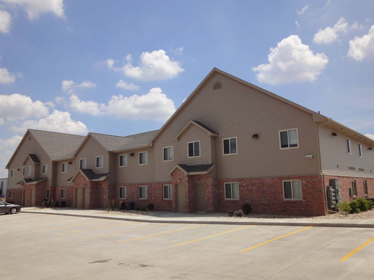 Apartment building with brick and beige siding under a partly cloudy sky.