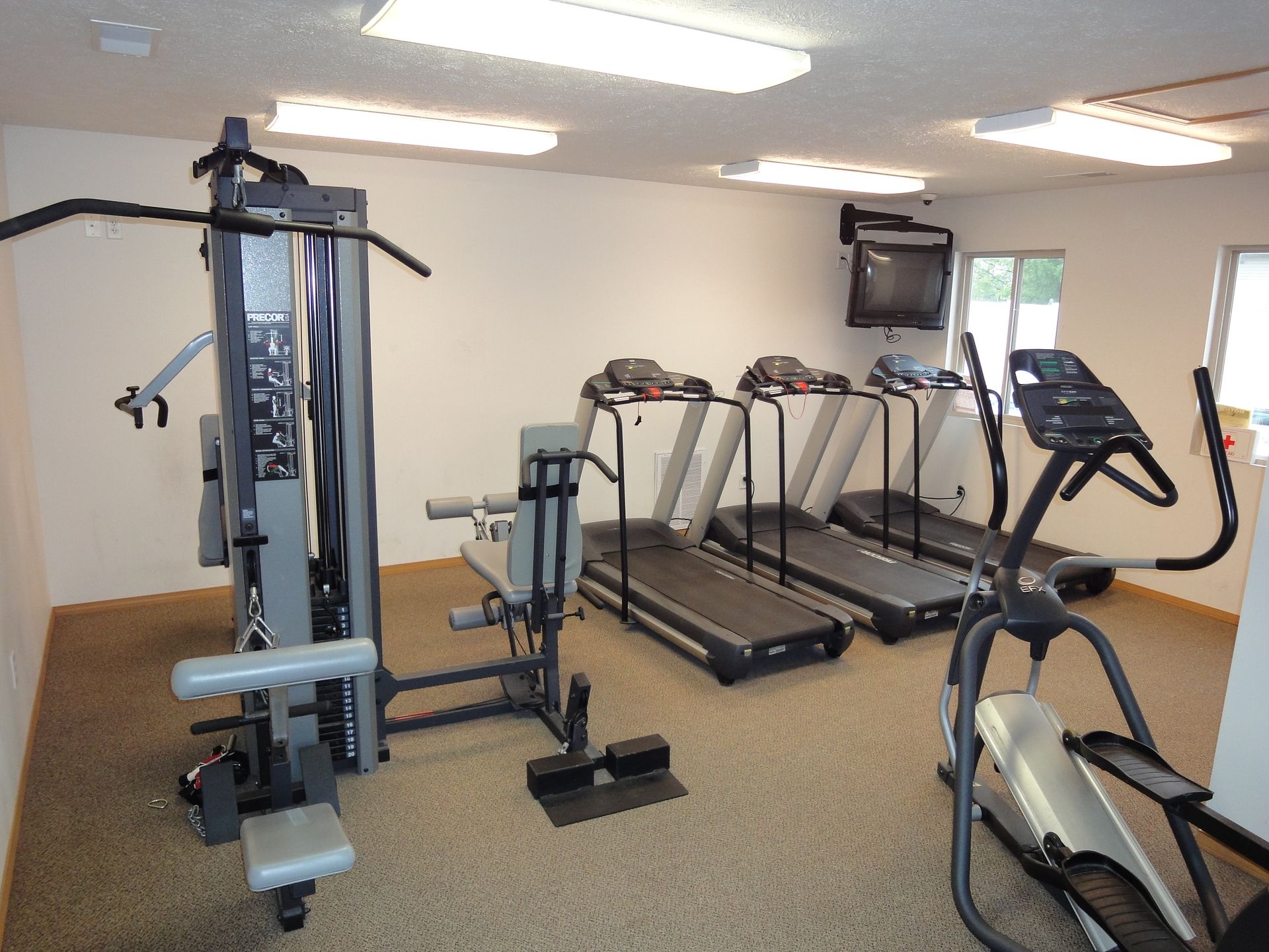 Gym interior with weight machine, treadmills, elliptical machine, and television.