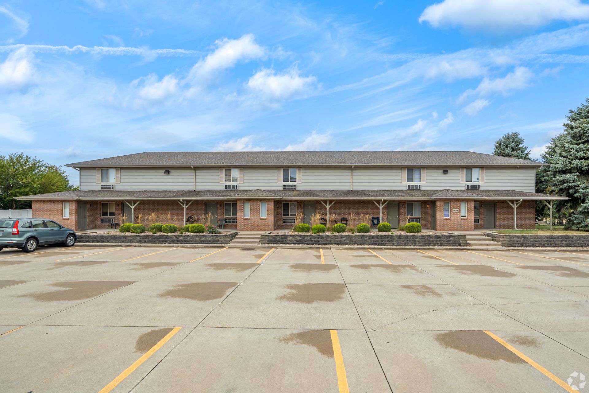 Apartment building with brick accents and a parking lot on a sunny day.