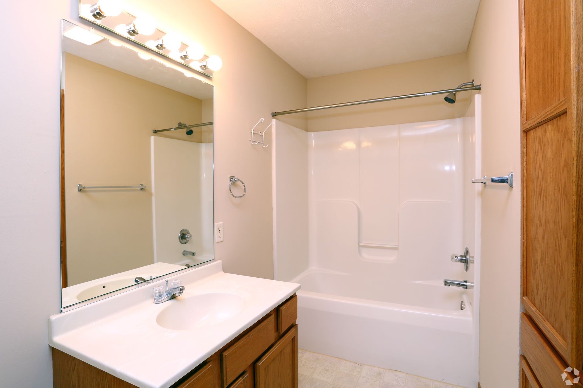 Bathroom with white tub/shower, vanity, mirror, and a wooden storage cabinet on the right.