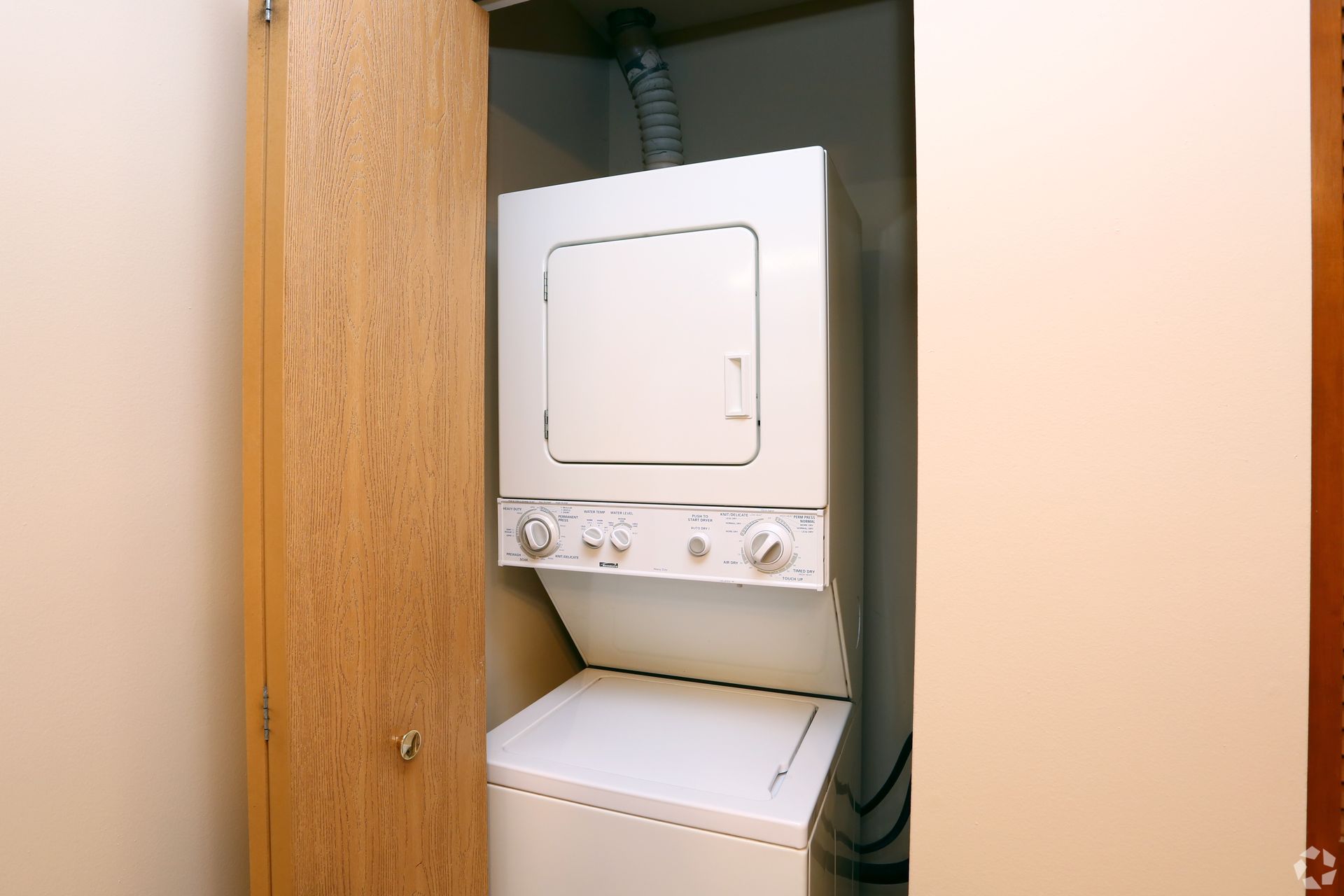 Stackable white washing machine and dryer in a closet.