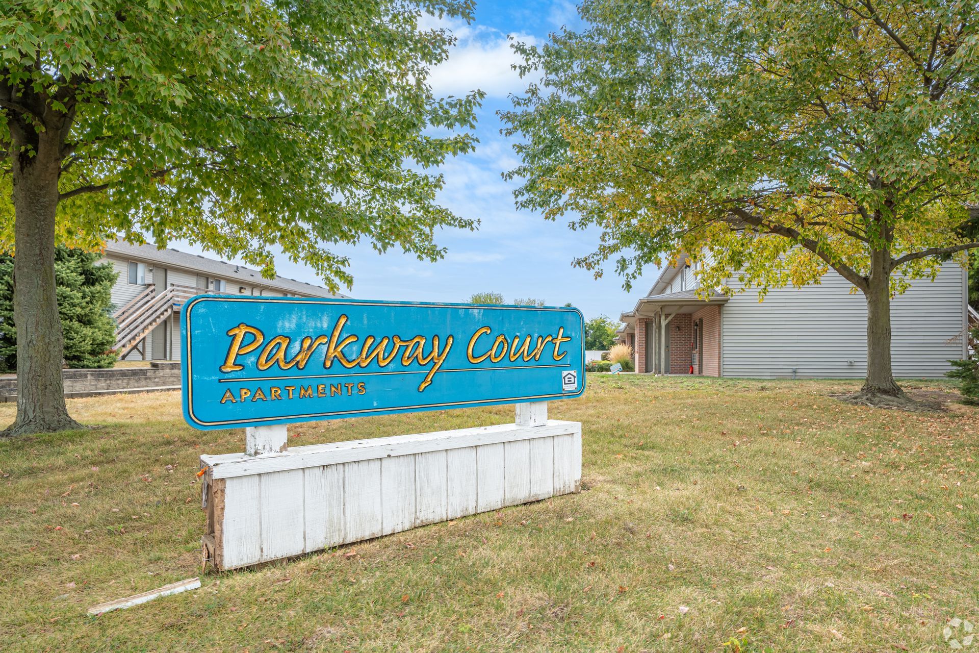 Sign for Parkway Court apartments on a grassy lawn with trees and buildings in the background.