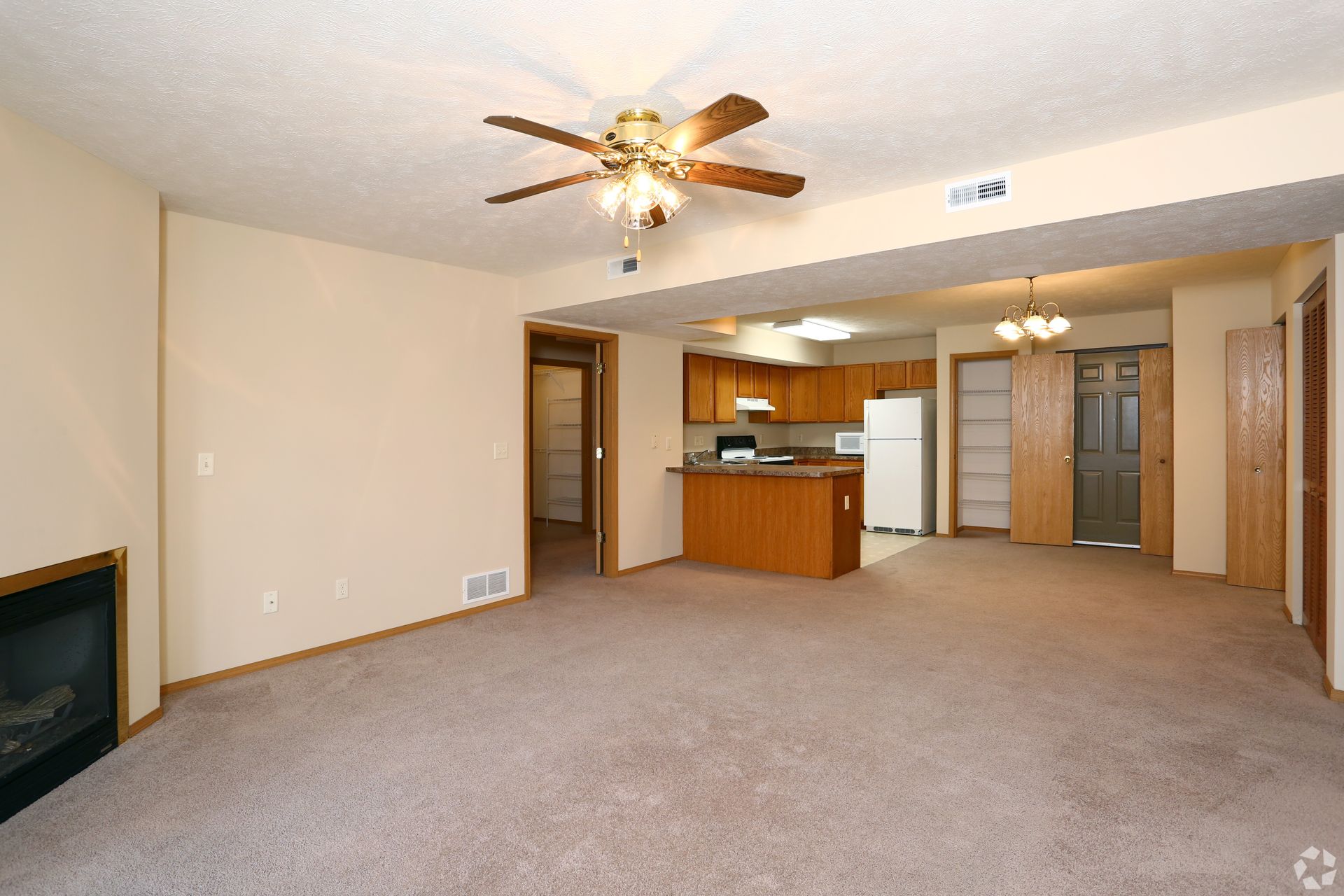 Living room with beige carpet, light brown walls, ceiling fan, and view into the kitchen.