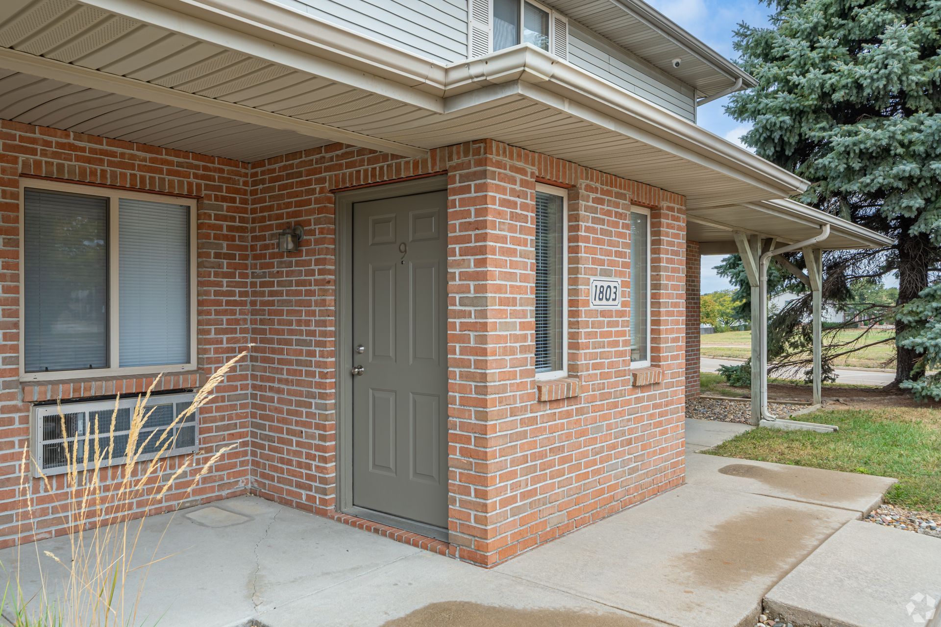 Brick apartment building entrance with a gray door and window.