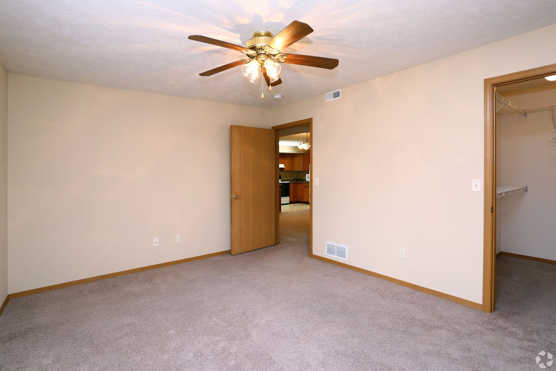 Bedroom with tan walls, brown carpet, ceiling fan, and open door to hallway and closet.