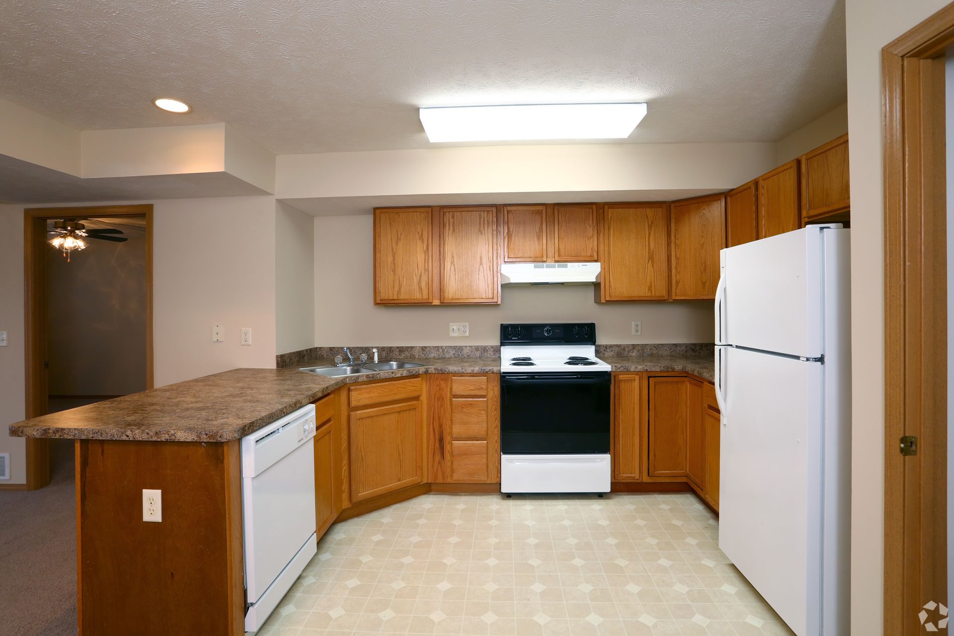 Kitchen with wooden cabinets, white appliances, and a breakfast bar.