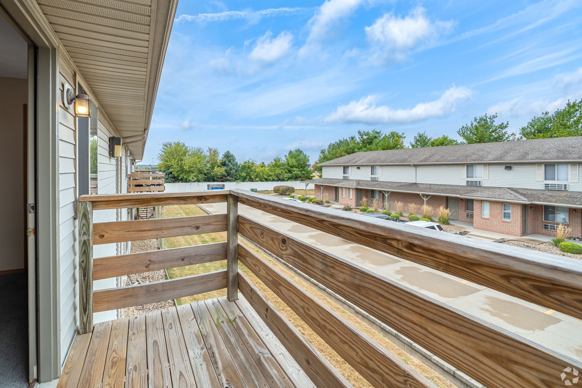 Balcony with wooden railing overlooking a row of apartments on a sunny day.