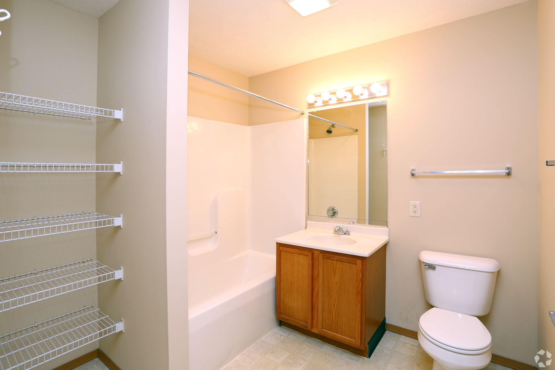 Bathroom with a white bathtub, toilet, and sink with wooden cabinet. Wire shelves on the left.
