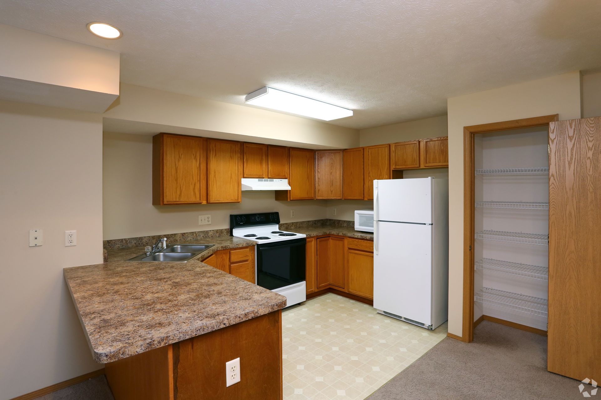 Kitchen with wooden cabinets, appliances, and island with countertop. Open pantry on right.