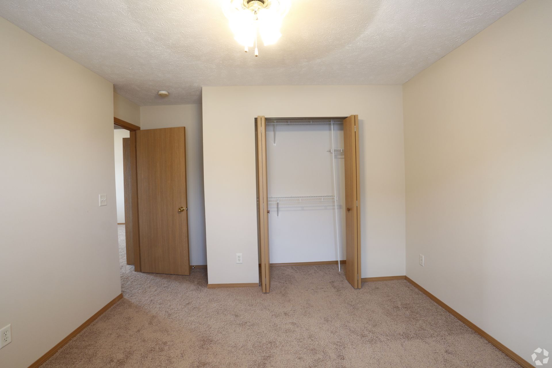 Empty bedroom with tan carpet, closet, and two doorways.