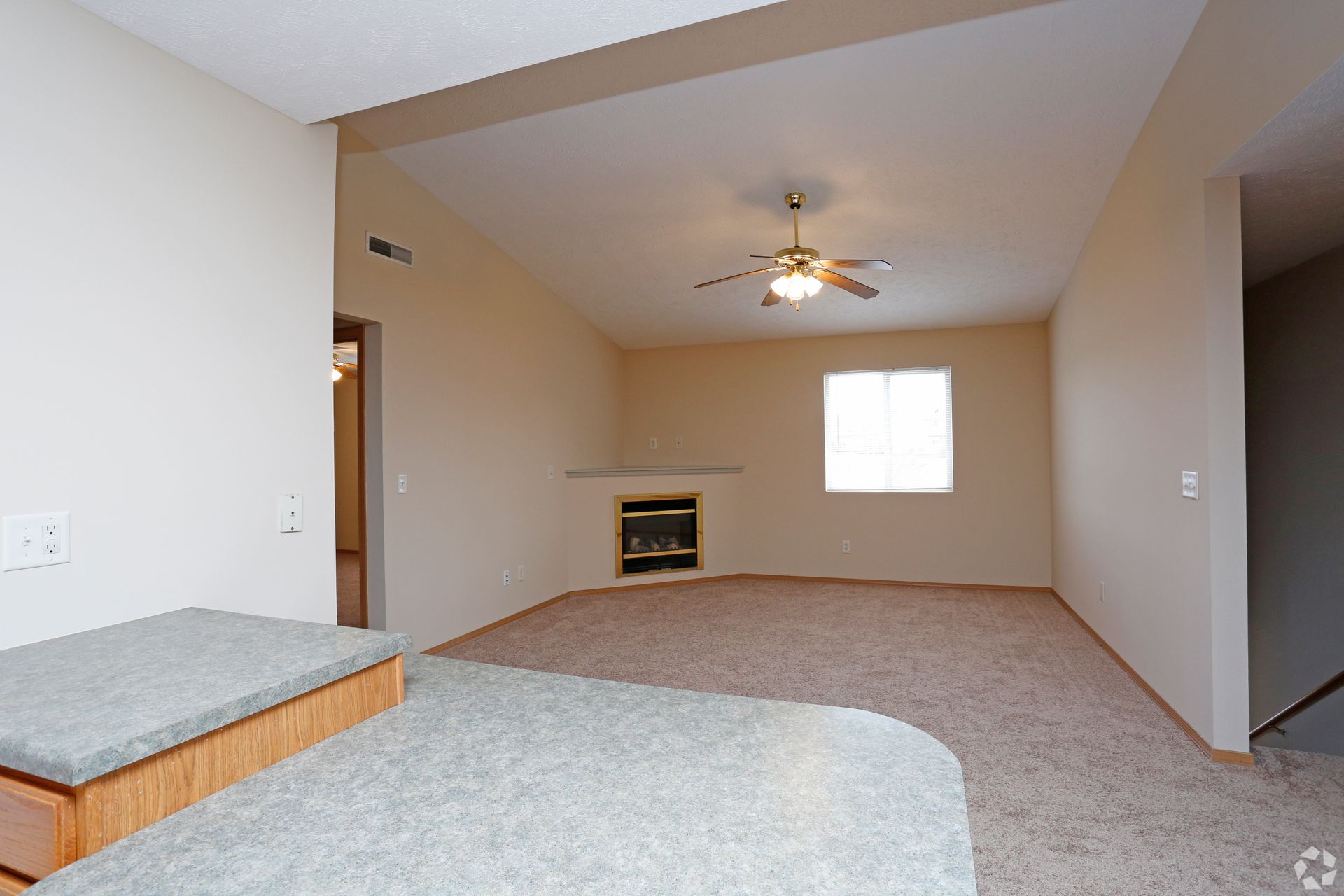 Interior view of a living room with a fireplace, window, and beige walls, with a kitchen countertop in the foreground.