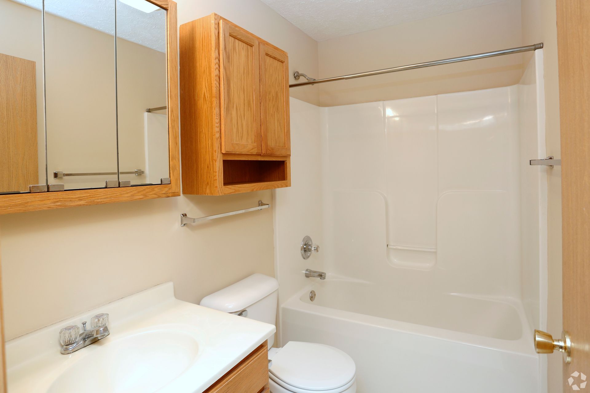 Bathroom with a tub, toilet, sink, mirror, and wooden cabinets.