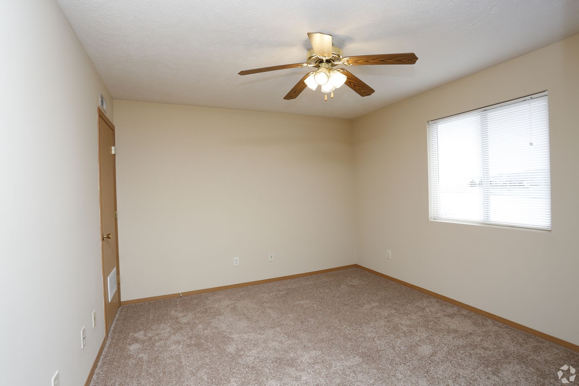 Empty room with brown carpet, tan walls, ceiling fan, window, and closed door.