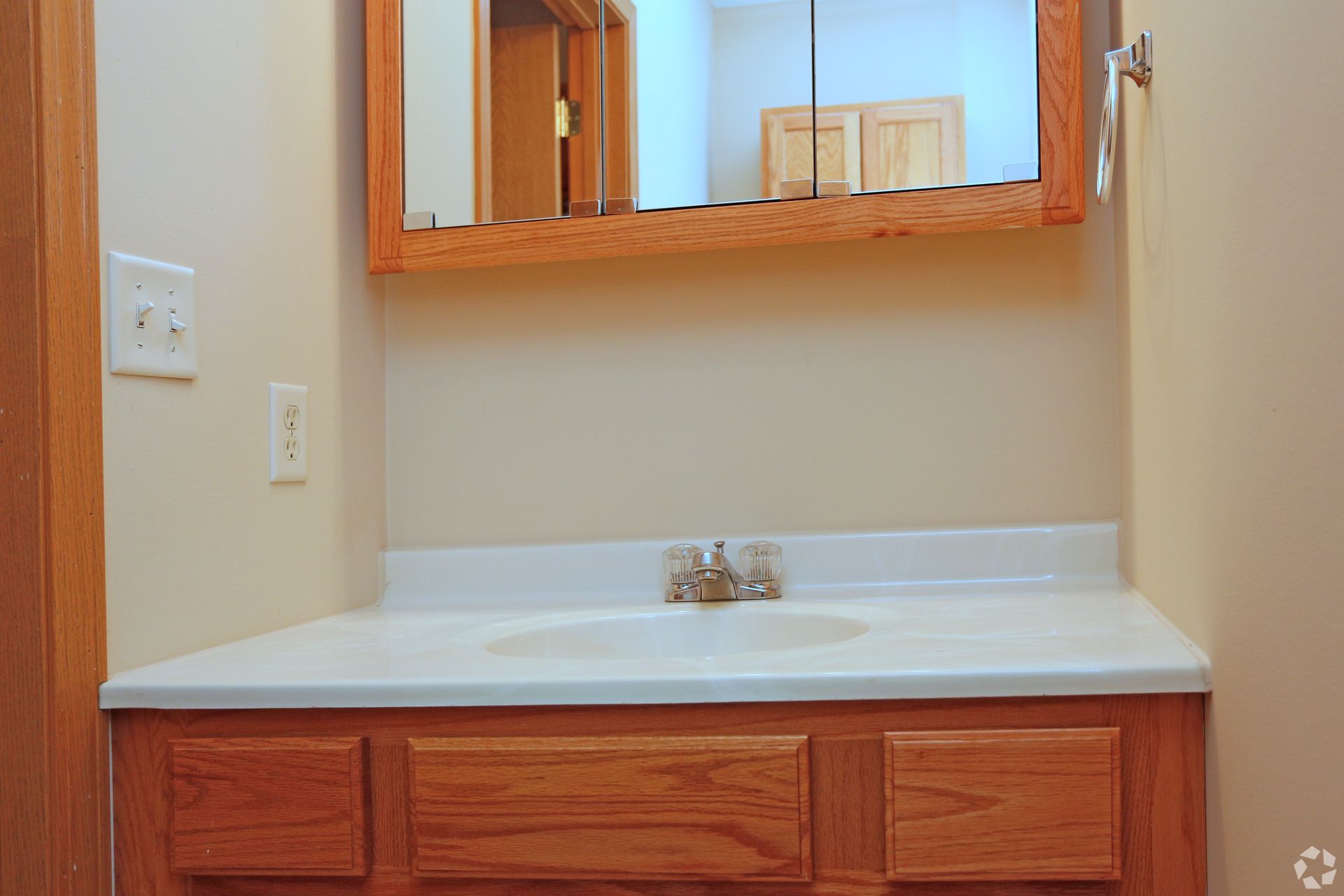 Bathroom vanity with oak cabinets, white countertop and sink, and a mirrored medicine cabinet.