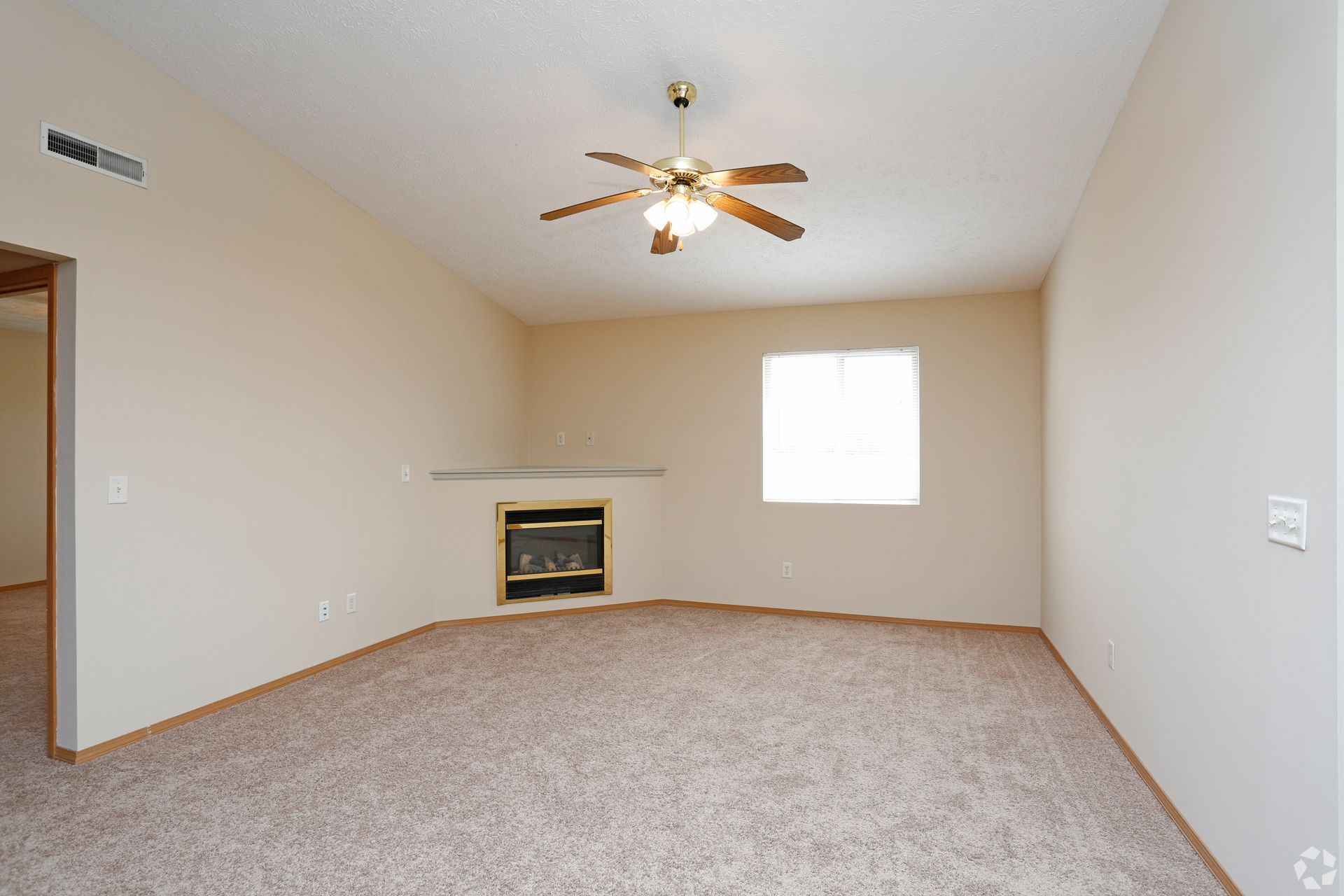 Empty room with beige walls, brown carpet, ceiling fan, fireplace, and window.