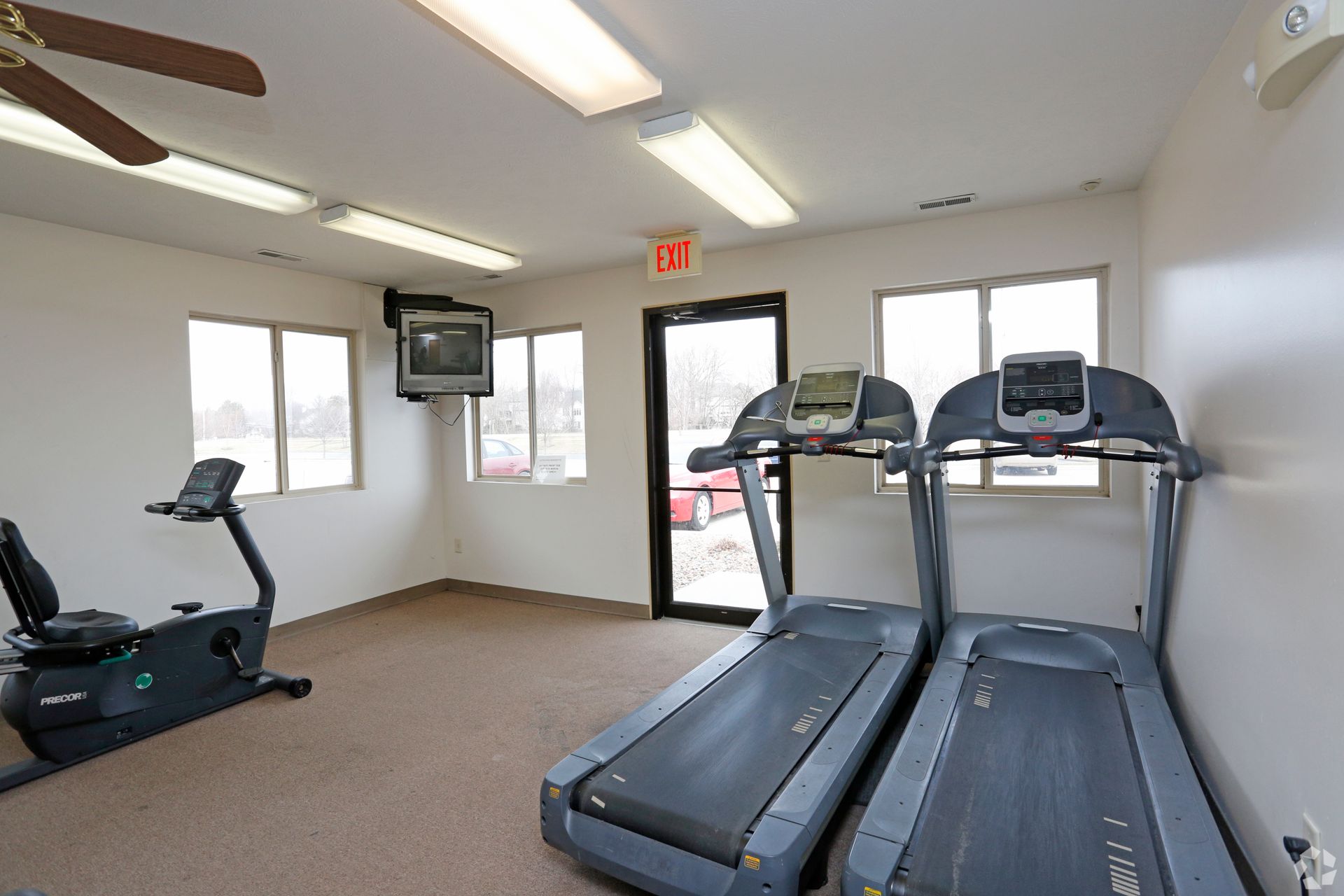 Gym with two treadmills, exercise bike, TV, door, and windows.