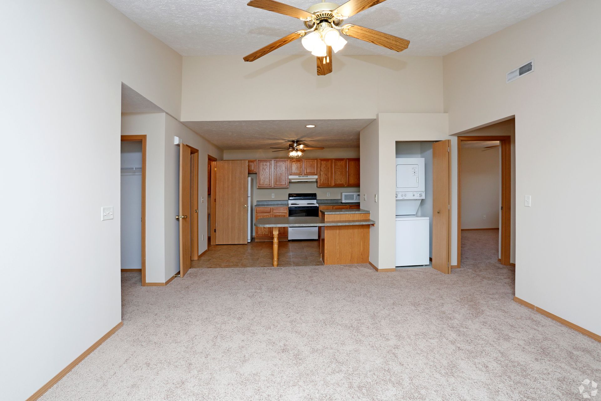 Interior of an apartment with light-colored walls, carpet, and a kitchen visible in the background.