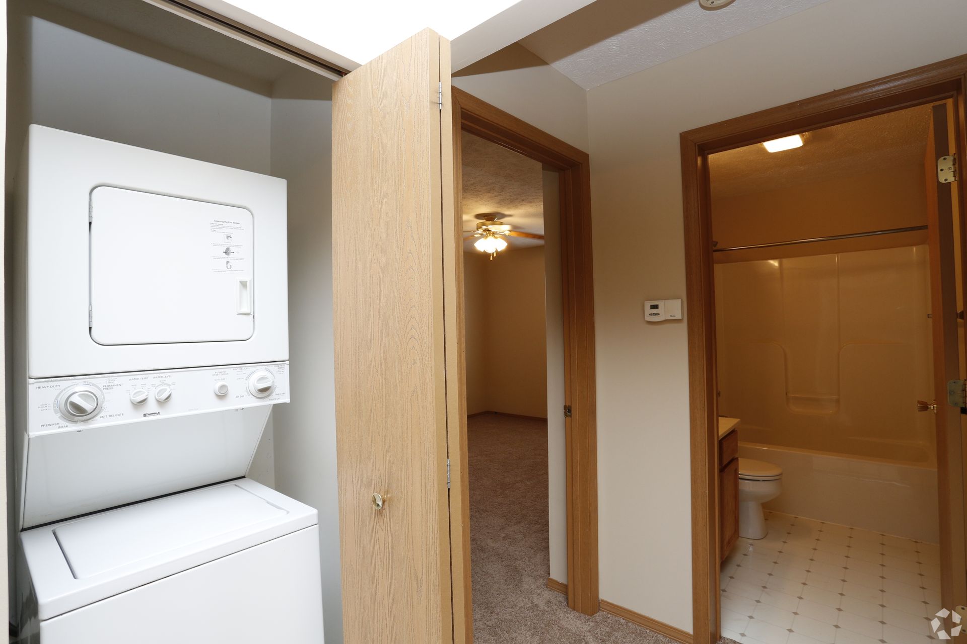 Laundry area with stacked white washer and dryer, and doorways leading to a bedroom and bathroom.