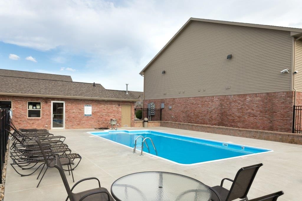 Swimming pool surrounded by buildings and lounge chairs under a cloudy sky.