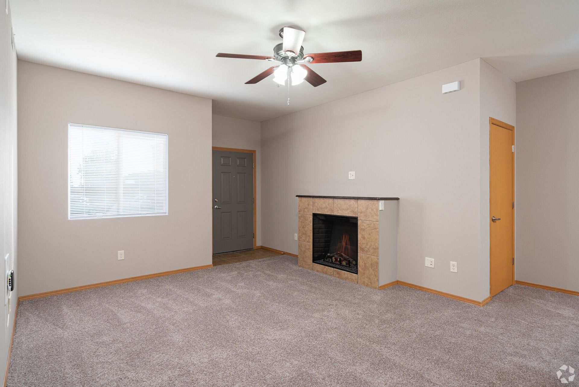Empty living room with carpet, fireplace, window, door, and ceiling fan.