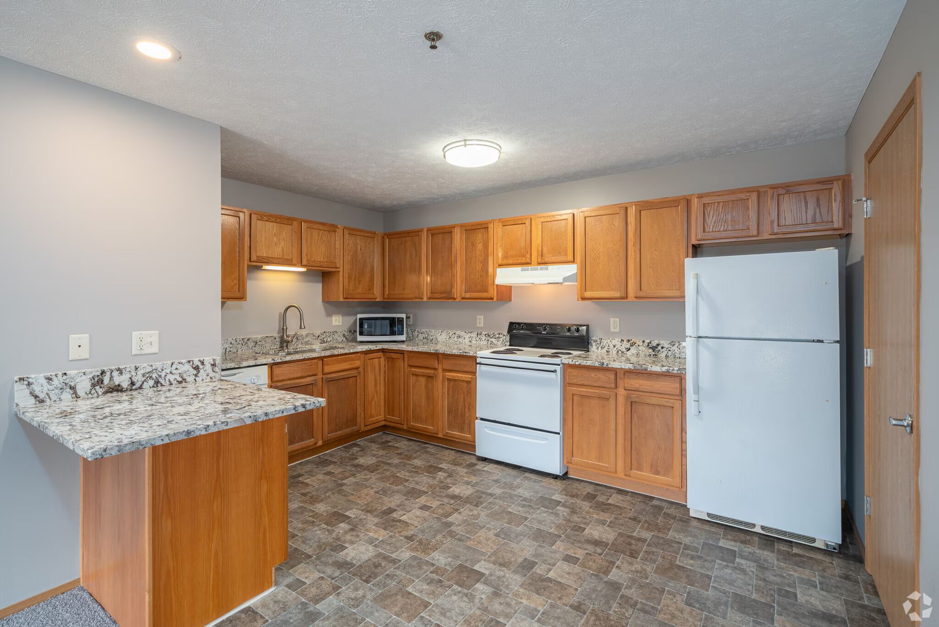 Kitchen with light-brown cabinets, countertops, and appliances. Includes a peninsula and flooring in neutral tones.