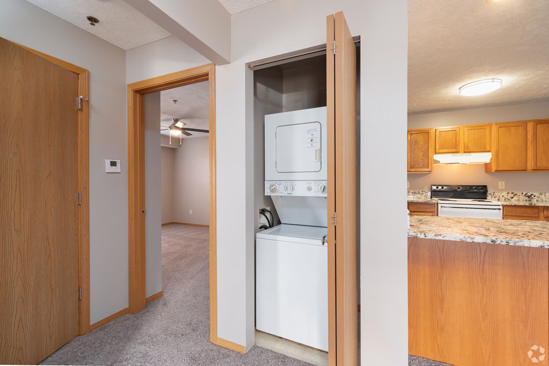 Apartment hallway with open closet housing a stacked washer and dryer, leading to a kitchen and living area.