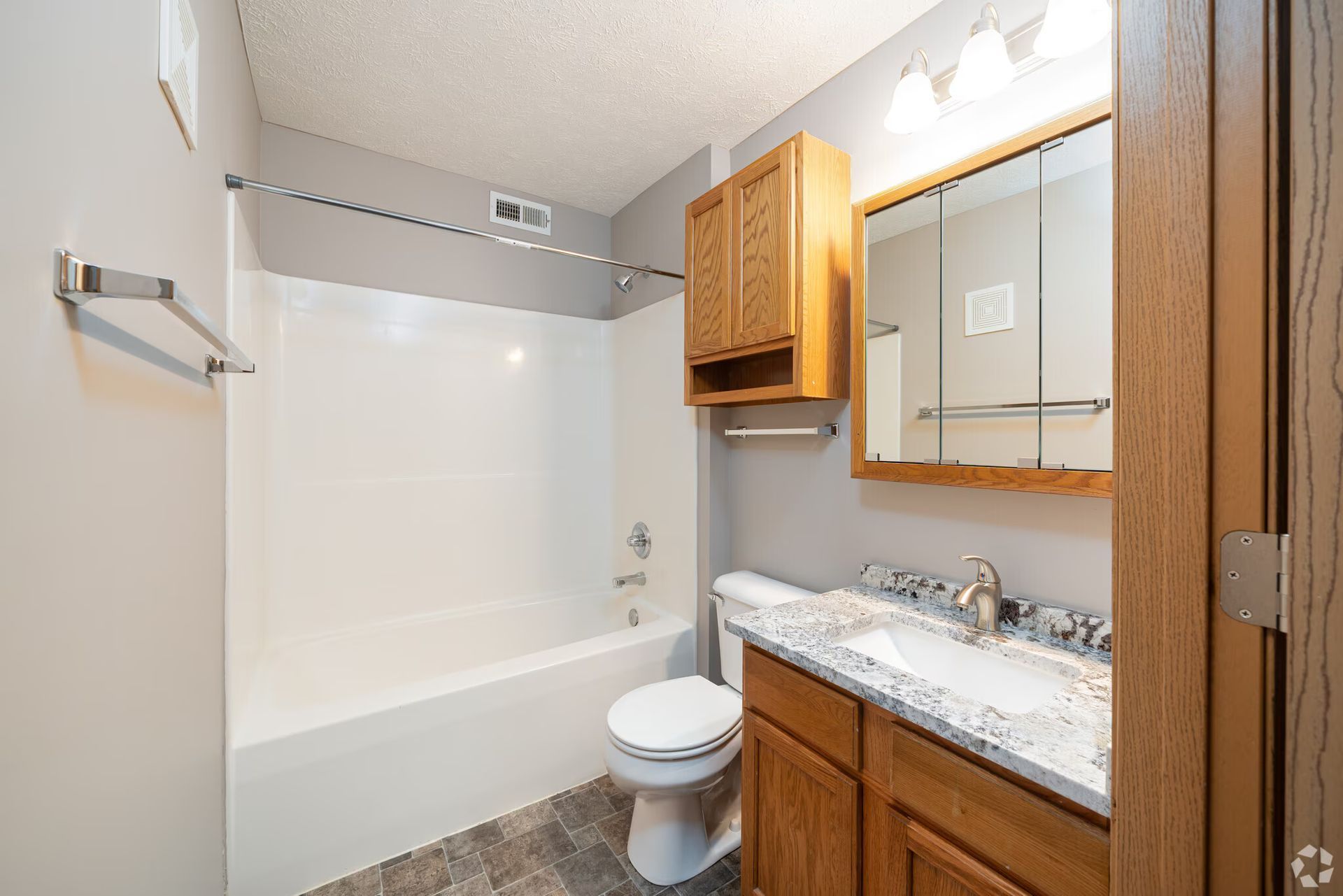 Bathroom with white tub, toilet, and vanity with a mirror and cabinet.