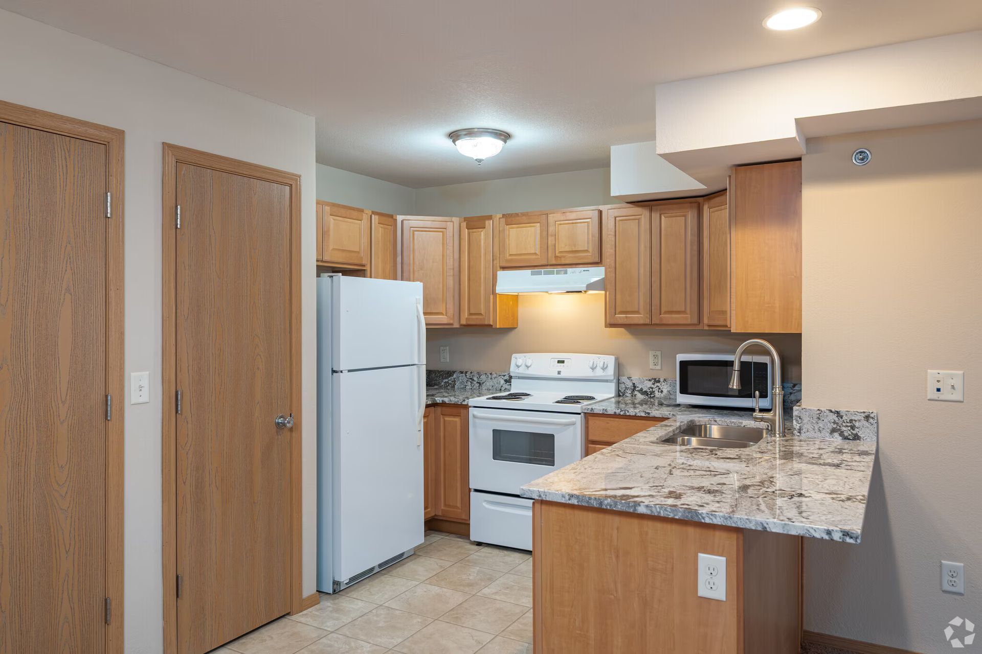 Kitchen with wood cabinets, white appliances, granite countertop, and tan walls.