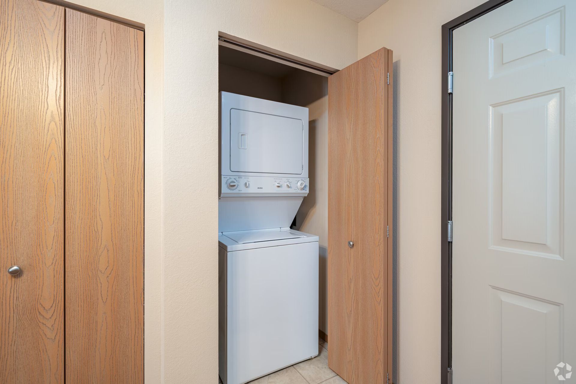 Washer and dryer unit in a closet between two wooden doors. White appliances, beige walls.