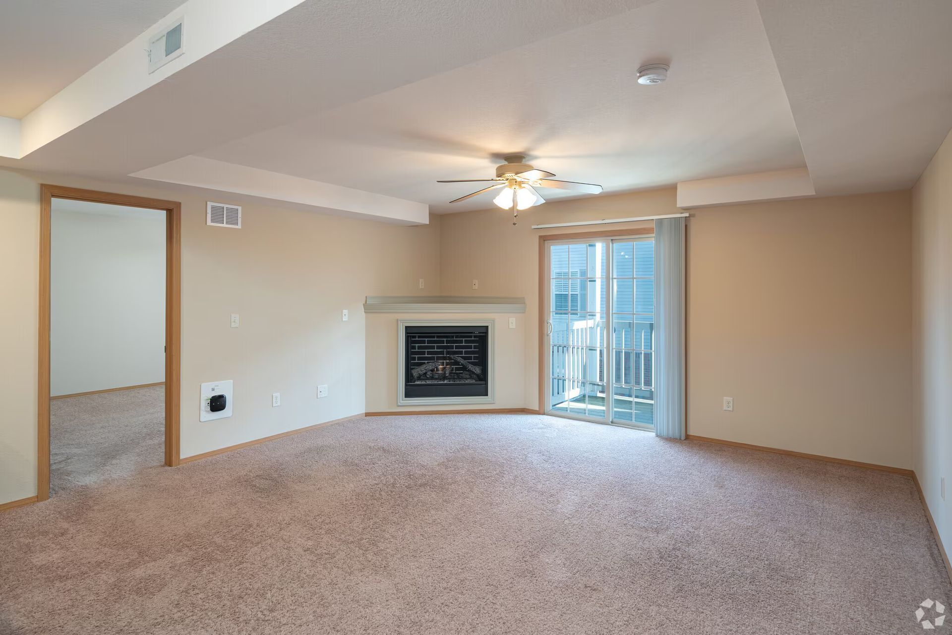 Empty living room with fireplace, sliding glass door to balcony, and tan carpet.