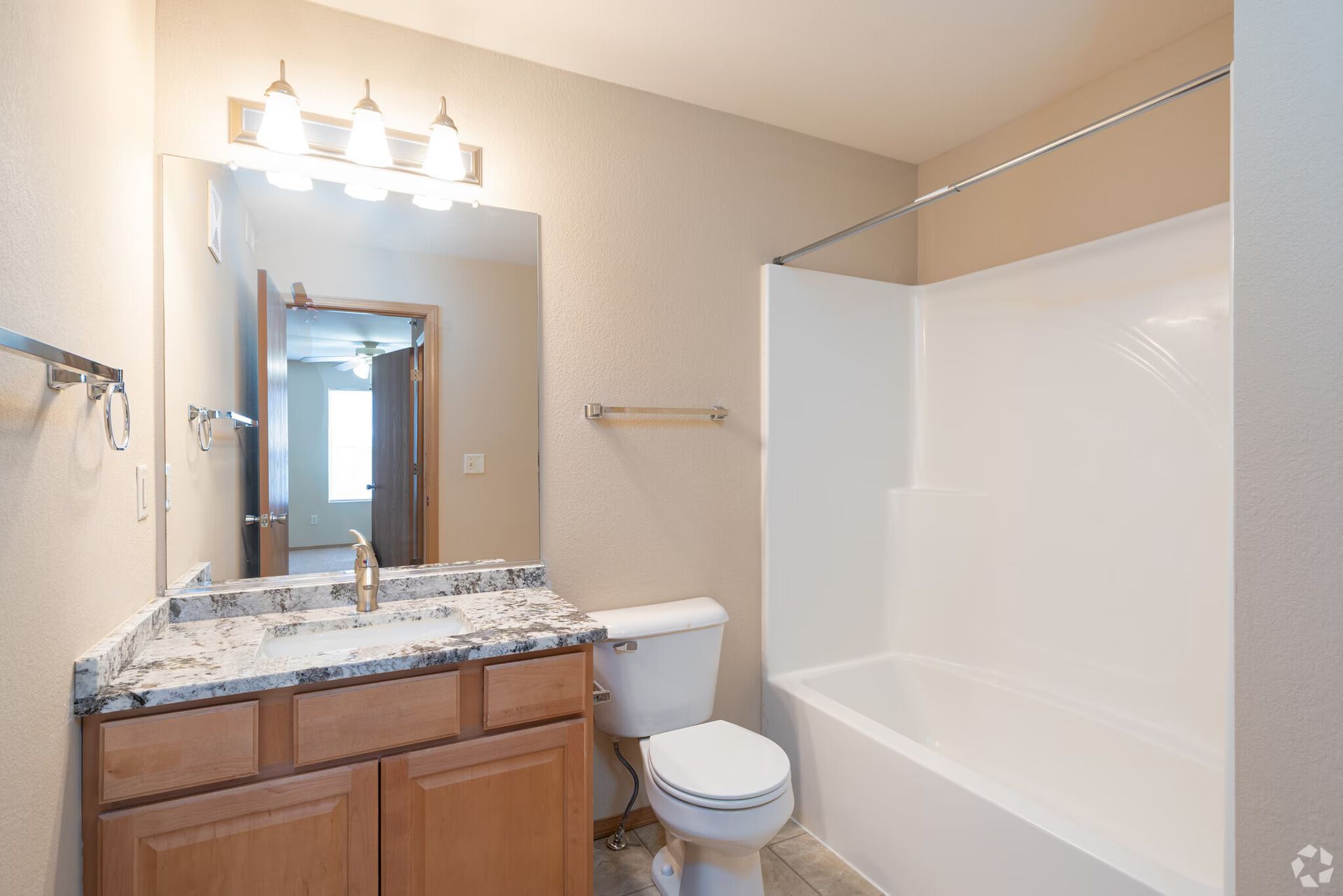 Bathroom with vanity, toilet, and bathtub. Light beige walls, wooden cabinet, and neutral-colored countertop.