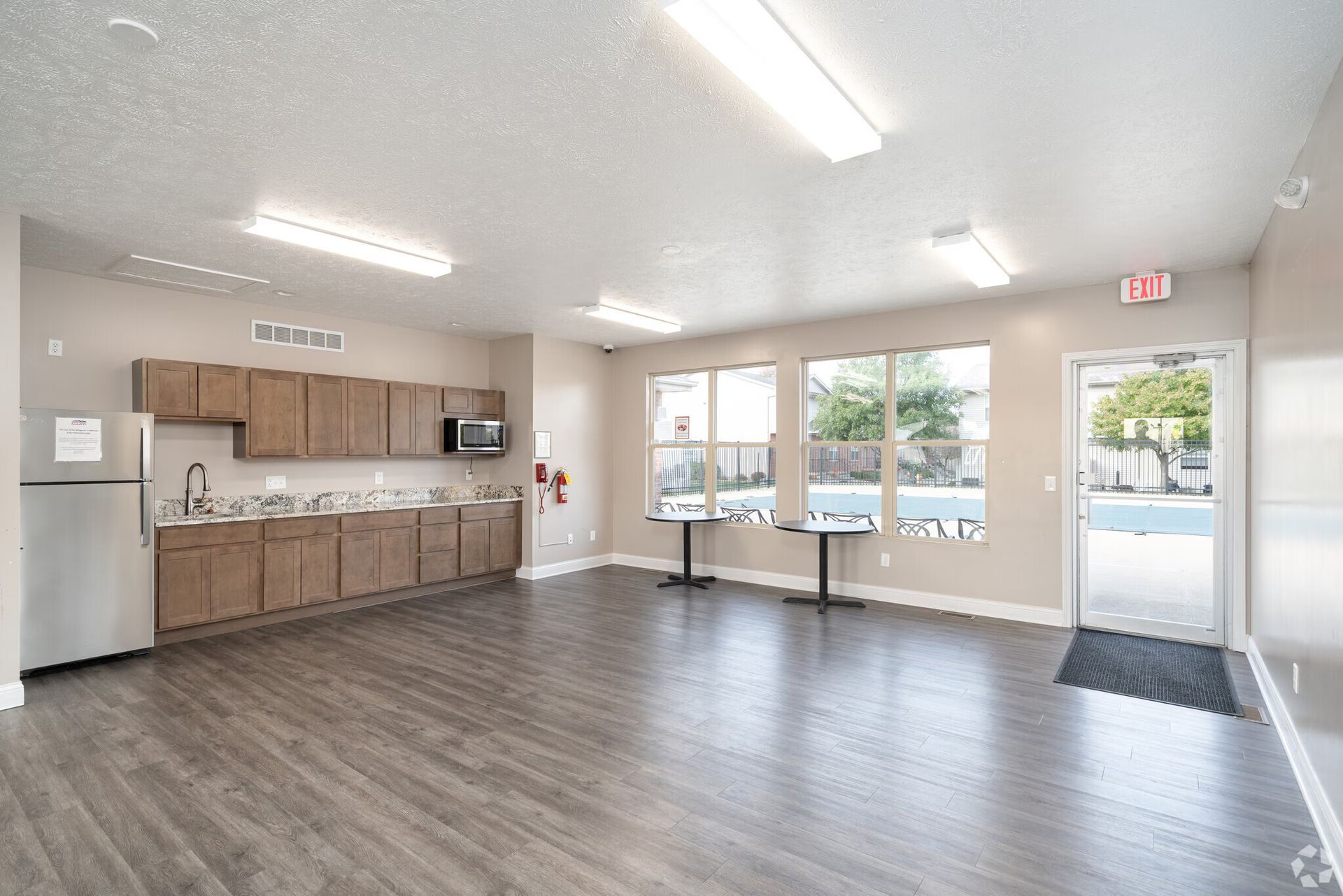 Community room with kitchenette, windows overlooking a pool, and wood-look flooring.