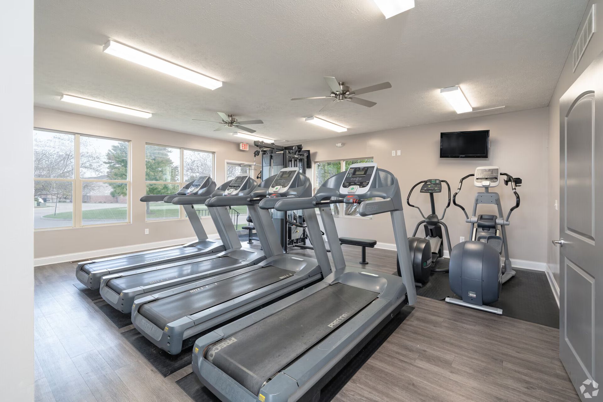 Gym with treadmills, elliptical machine, weight machine, television, and windows.