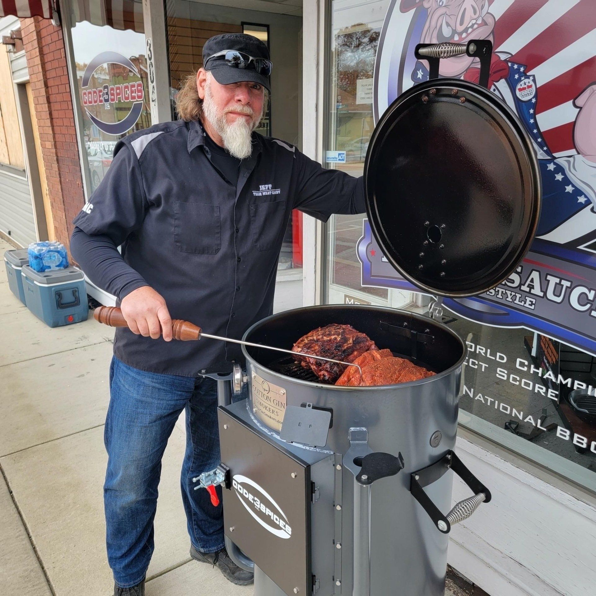 A man is standing next to a grill with the lid open